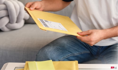 Hände einer sitzenden Person, die einen Großbrief hält.